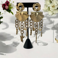 Vintage 1980s French stamped brass dangle earrings featuring a scallop shell centerpiece with eclectic dangling charms, including an owl, shovel, putti angel, axe, and scissors. Unique statement jewelry with a bold boho style, rich patina, and artistic character.