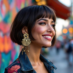 Vintage 1980s French stamped brass dangle earrings featuring a scallop shell centerpiece with eclectic dangling charms, including an owl, shovel, putti angel, axe, and scissors. Unique statement jewelry with a bold boho style, rich patina, and artistic character.
