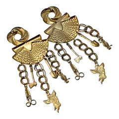 Vintage 1980s French stamped brass dangle earrings featuring a scallop shell centerpiece with eclectic dangling charms, including an owl, shovel, putti angel, axe, and scissors. Unique statement jewelry with a bold boho style, rich patina, and artistic character.