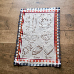 French jacquard cotton tea towel in beige, orange, and blue featuring illustrations of traditional French breads with “Pains de Tradition Française” lettering. Made in France.