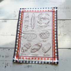 French jacquard cotton tea towel in beige, orange, and blue featuring illustrations of traditional French breads with “Pains de Tradition Française” lettering. Made in France.