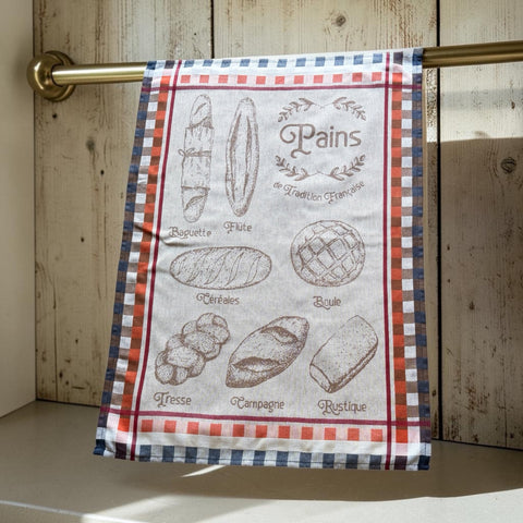 French jacquard cotton tea towel in beige, orange, and blue featuring illustrations of traditional French breads with “Pains de Tradition Française” lettering. Made in France.