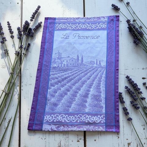 French jacquard cotton tea towel in lavender, violet, and white featuring Provençal lavender fields, farmhouse, and “La Provence” lettering. Made in France.