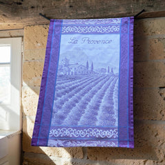 French jacquard cotton tea towel in lavender, violet, and white featuring Provençal lavender fields, farmhouse, and “La Provence” lettering. Made in France.
