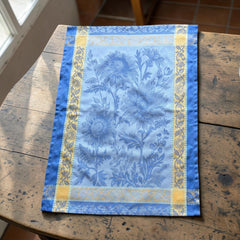 French jacquard cotton tea towel in sky blue and golden yellow featuring woven sunflower design and ornate border.