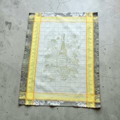 French jacquard cotton tea towel in green, yellow, and soft gray featuring a Le Vieux Chêne wine bottle surrounded by grapes and vine leaves.