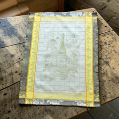 French jacquard cotton tea towel in green, yellow, and soft gray featuring a Le Vieux Chêne wine bottle surrounded by grapes and vine leaves.
