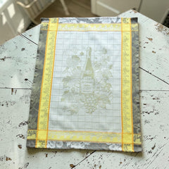 French jacquard cotton tea towel in green, yellow, and soft gray featuring a Le Vieux Chêne wine bottle surrounded by grapes and vine leaves.