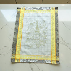 French jacquard cotton tea towel in green, yellow, and soft gray featuring a Le Vieux Chêne wine bottle surrounded by grapes and vine leaves.