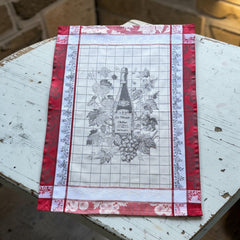 French jacquard cotton tea towel in red, white, and soft gray beige featuring a Le Vieux Chêne wine bottle surrounded by grapes and vine leaves.