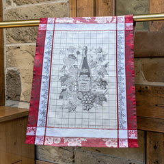 French jacquard cotton tea towel in red, white, and soft gray beige featuring a Le Vieux Chêne wine bottle surrounded by grapes and vine leaves.