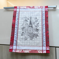 French jacquard cotton tea towel in red, white, and soft gray beige featuring a Le Vieux Chêne wine bottle surrounded by grapes and vine leaves.