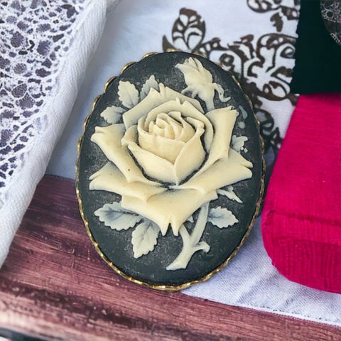 A lovely vintage French faux cameo scarf/dress clip from the late 1950s or early 1960s. Featuring a cream-colored high relief rose set against a black background, encased in a scalloped gold-tone bezel. The hammered gold frame adds texture, while the clip at the back ensures secure attachment to scarves, dresses, or lapels. Marked '3S' on the back, though the maker is unknown. A timeless and elegant accessory, perfect for vintage lovers and sustainable fashion enthusiasts.