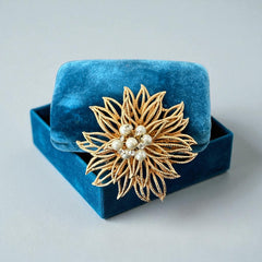 Vintage 1960s gold-tone floral brooch with openwork textured petals, featuring faux pearls and clear rhinestones on headpins at the center.