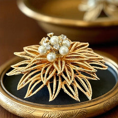 Vintage 1960s gold-tone floral brooch with openwork textured petals, featuring faux pearls and clear rhinestones on headpins at the center.