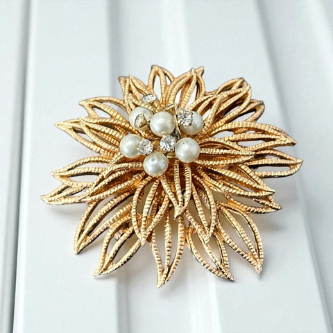 Vintage 1960s gold-tone floral brooch with openwork textured petals, featuring faux pearls and clear rhinestones on headpins at the center.
