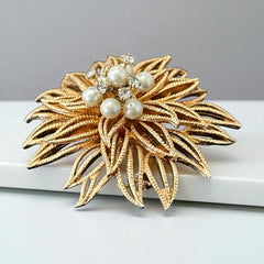 Vintage 1960s gold-tone floral brooch with openwork textured petals, featuring faux pearls and clear rhinestones on headpins at the center.