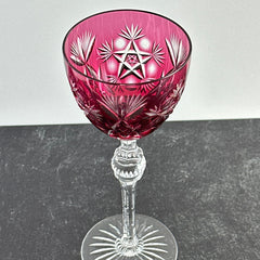 Vintage cranberry cut crystal goblet with geometric star and fan cuts, faceted clear stem, and round foot.