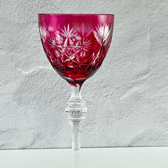 Vintage cranberry cut crystal goblet with geometric star and fan cuts, faceted clear stem, and round foot.