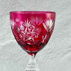 Vintage cranberry cut crystal goblet with geometric star and fan cuts, faceted clear stem, and round foot.