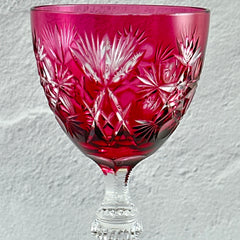 Vintage cranberry cut crystal goblet with geometric star and fan cuts, faceted clear stem, and round foot.