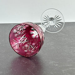 Vintage cranberry cut crystal goblet with geometric star and fan cuts, faceted clear stem, and round foot.