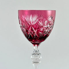 Vintage cranberry cut crystal goblet with geometric star and fan cuts, faceted clear stem, and round foot.