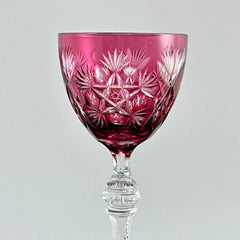 Vintage cranberry cut crystal goblet with geometric star and fan cuts, faceted clear stem, and round foot.