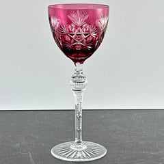 Vintage cranberry cut crystal goblet with geometric star and fan cuts, faceted clear stem, and round foot.