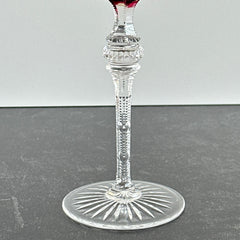 Vintage cranberry cut crystal goblet with geometric star and fan cuts, faceted clear stem, and round foot.
