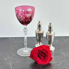 Vintage cranberry cut crystal goblet with geometric star and fan cuts, faceted clear stem, and round foot.