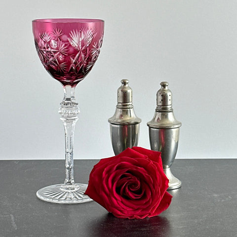 Vintage cranberry cut crystal goblet with geometric star and fan cuts, faceted clear stem, and round foot.