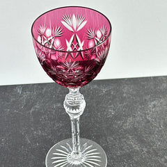 Vintage cranberry cut crystal goblet with geometric star and fan cuts, faceted clear stem, and round foot.