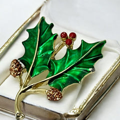 Vintage Gerry’s holly brooch with red enamel berries and metallic green enamel leaves on a gold-tone stem; signed Gerry’s on the back, 1980s holiday jewelry in very good condition with minor enamel wear.