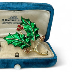 Vintage Gerry’s holly brooch with red enamel berries and metallic green enamel leaves on a gold-tone stem; signed Gerry’s on the back, 1980s holiday jewelry in very good condition with minor enamel wear.
