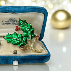 Vintage Gerry’s holly brooch with red enamel berries and metallic green enamel leaves on a gold-tone stem; signed Gerry’s on the back, 1980s holiday jewelry in very good condition with minor enamel wear.