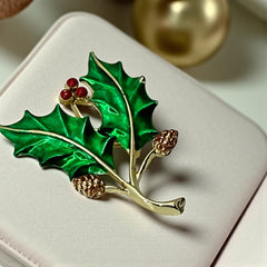 Vintage Gerry’s holly brooch with red enamel berries and metallic green enamel leaves on a gold-tone stem; signed Gerry’s on the back, 1980s holiday jewelry in very good condition with minor enamel wear.