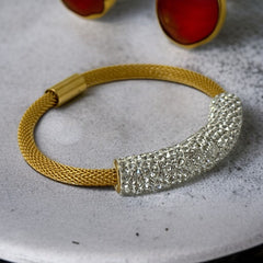 Gold tone mesh bracelet with a curved white centerpiece set with clear rhinestones over silver foil backing, creating a bright silvery shimmer; finished with a magnetic clasp and sleek modern design.