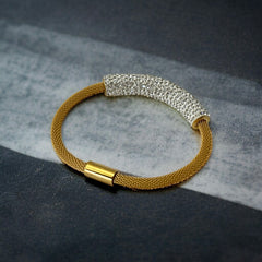 Gold tone mesh bracelet with a curved white centerpiece set with clear rhinestones over silver foil backing, creating a bright silvery shimmer; finished with a magnetic clasp and sleek modern design.