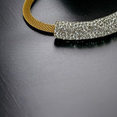 Gold tone mesh bracelet with a curved white centerpiece set with clear rhinestones over silver foil backing, creating a bright silvery shimmer; finished with a magnetic clasp and sleek modern design.