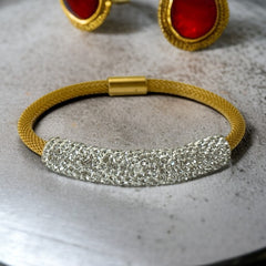 Gold tone mesh bracelet with a curved white centerpiece set with clear rhinestones over silver foil backing, creating a bright silvery shimmer; finished with a magnetic clasp and sleek modern design.