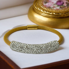 Gold tone mesh bracelet with a curved white centerpiece set with clear rhinestones over silver foil backing, creating a bright silvery shimmer; finished with a magnetic clasp and sleek modern design.