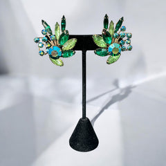 Vintage 1960s clip-on floral earrings with green and iridescent rhinestones in chaton, navette, and marquise cuts, set in gold-tone metal—sparkling midcentury costume jewelry in very good condition.