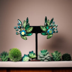 Vintage 1960s clip-on floral earrings with green and iridescent rhinestones in chaton, navette, and marquise cuts, set in gold-tone metal—sparkling midcentury costume jewelry in very good condition.