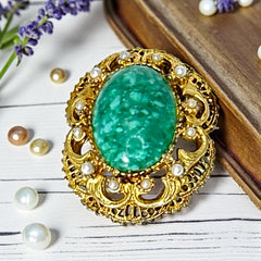 Vintage brooch pendant with mottled green glass cabochon, faux pearls, and ornate gold tone filigree, photographed front and back to highlight its 1960s–70s revival style and dual-wear functionality.