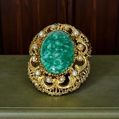 Vintage brooch pendant with mottled green glass cabochon, faux pearls, and ornate gold tone filigree, photographed front and back to highlight its 1960s–70s revival style and dual-wear functionality.