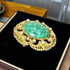 Vintage brooch pendant with mottled green glass cabochon, faux pearls, and ornate gold tone filigree, photographed front and back to highlight its 1960s–70s revival style and dual-wear functionality.