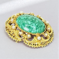 Vintage brooch pendant with mottled green glass cabochon, faux pearls, and ornate gold tone filigree, photographed front and back to highlight its 1960s–70s revival style and dual-wear functionality.