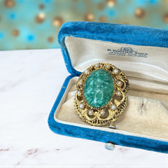 Vintage brooch pendant with mottled green glass cabochon, faux pearls, and ornate gold tone filigree, photographed front and back to highlight its 1960s–70s revival style and dual-wear functionality.