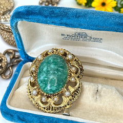 Vintage brooch pendant with mottled green glass cabochon, faux pearls, and ornate gold tone filigree, photographed front and back to highlight its 1960s–70s revival style and dual-wear functionality.